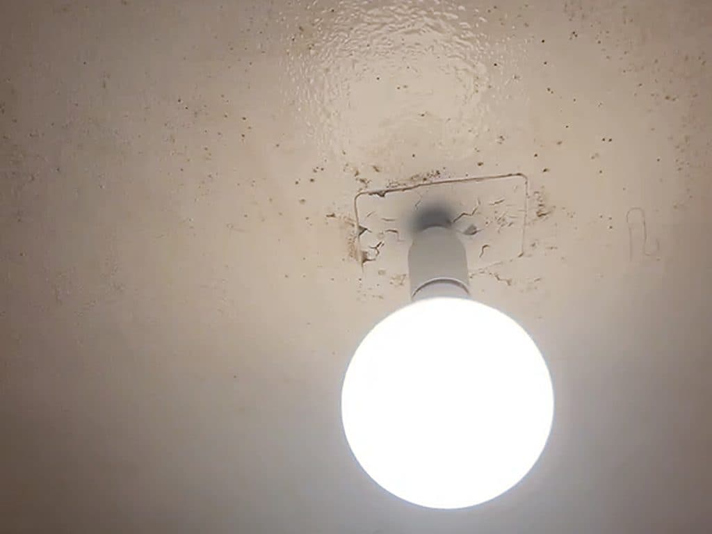 Cielo de baño con la pintura agrietada y suelta alrededor de la lámpara, antes de repararlo y pintarlo