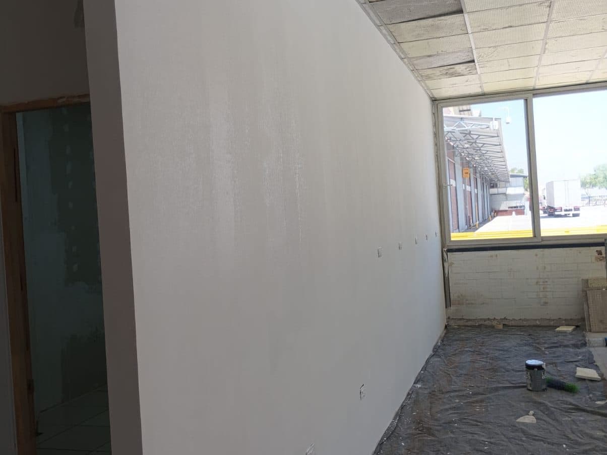 Muro largo recién pintado, con el piso cubierto con plástico