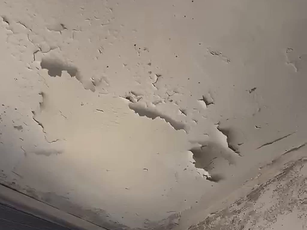 Cielo con la pintura descascarada y agrietada en la esquina de la ventana, antes de repararlo y pintarlo