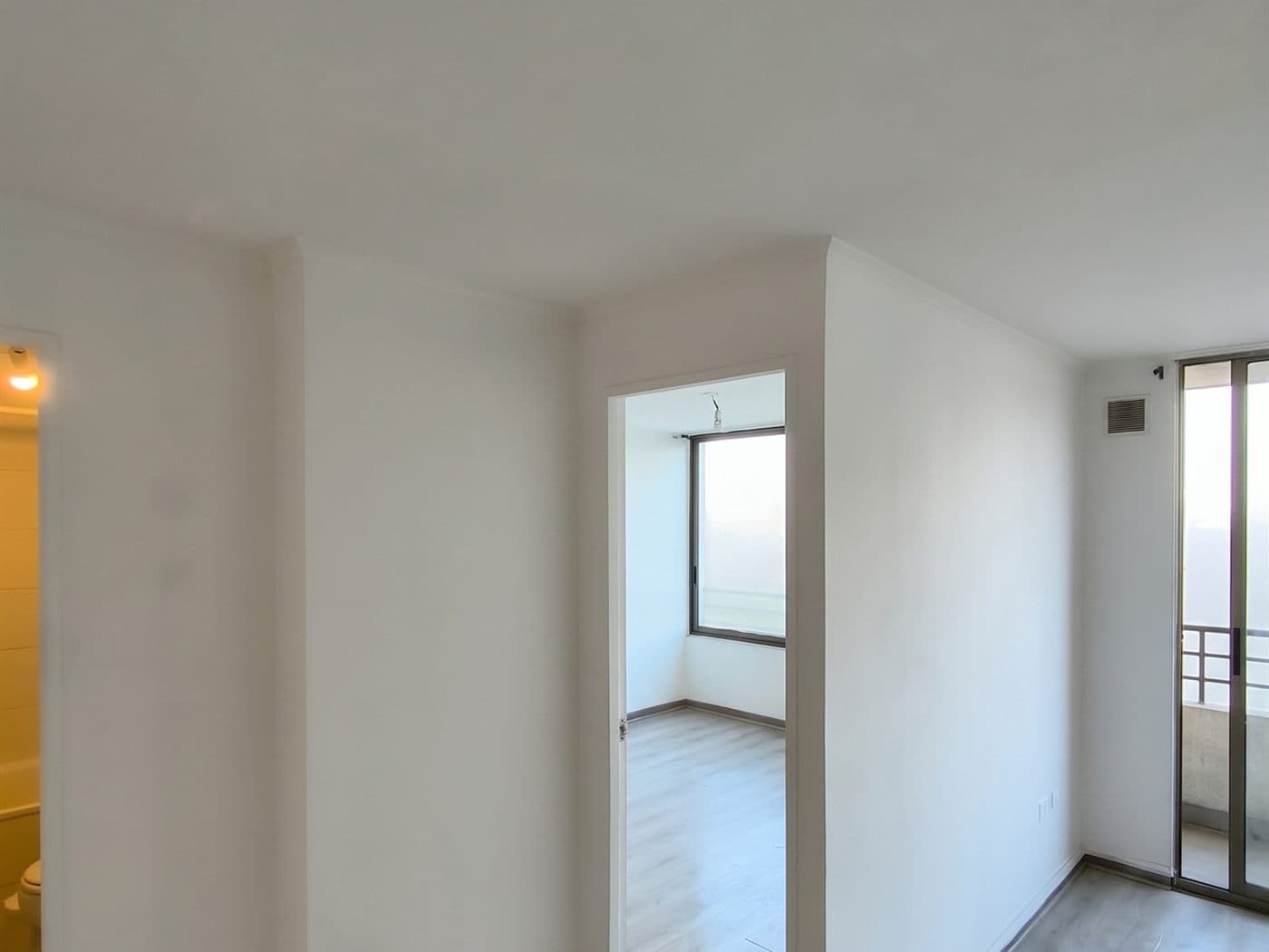 Pasillo y dormitorio de un depto desocupado con los muros recién pintados de blanco para la entrega
