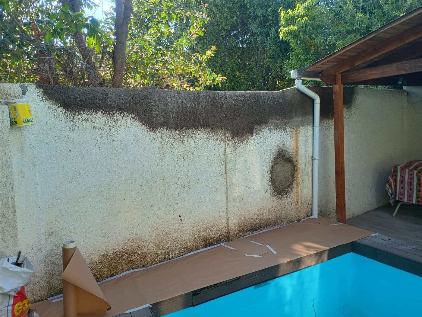Muralla del patio junto a la piscina, con hongos negros en la parte alta y manchas de humedad, antes de repararla